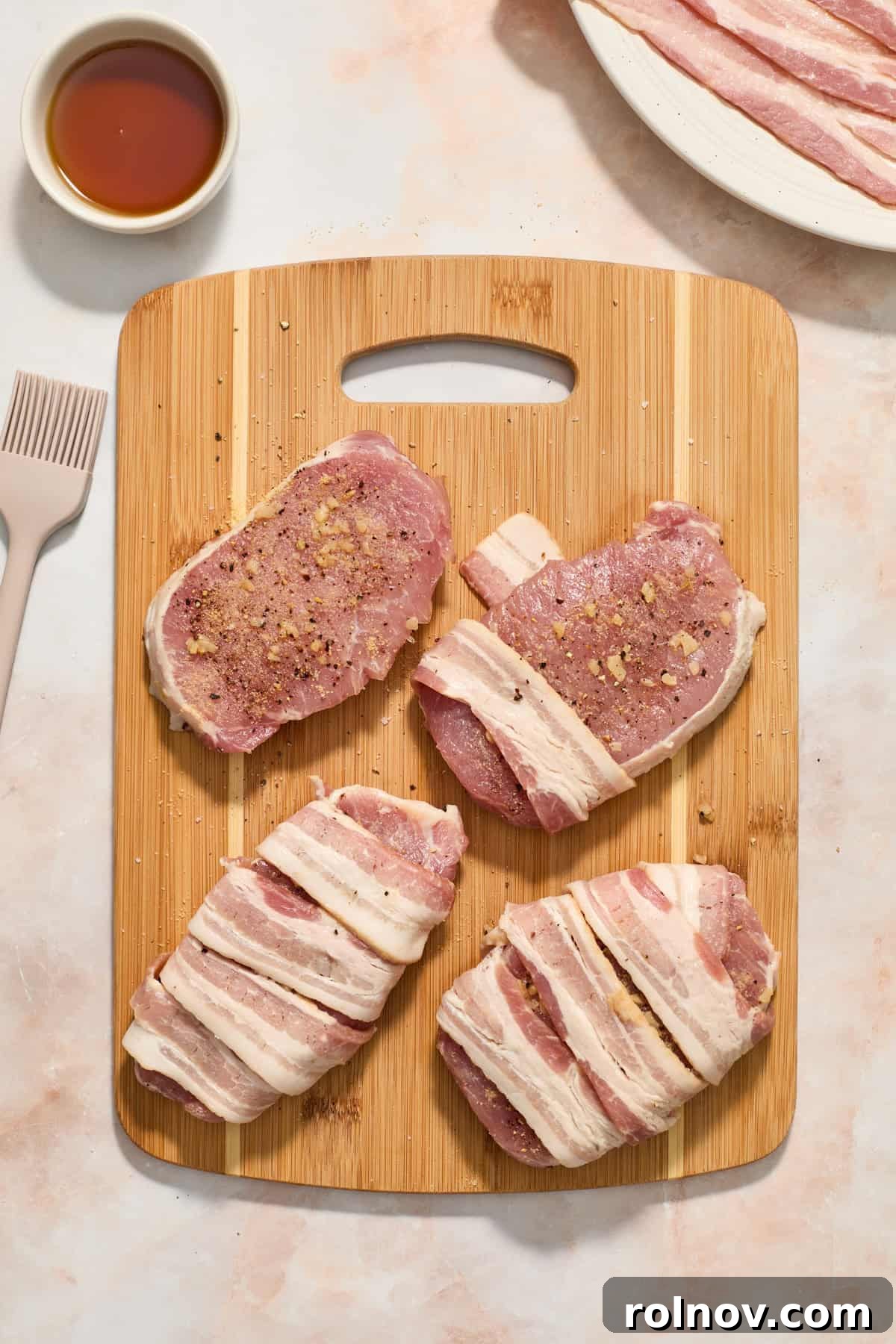 Sweet and Savory Maple Bacon Pork Chops 6 Pork chops with bacon strips carefully wrapped around them on a cutting board.