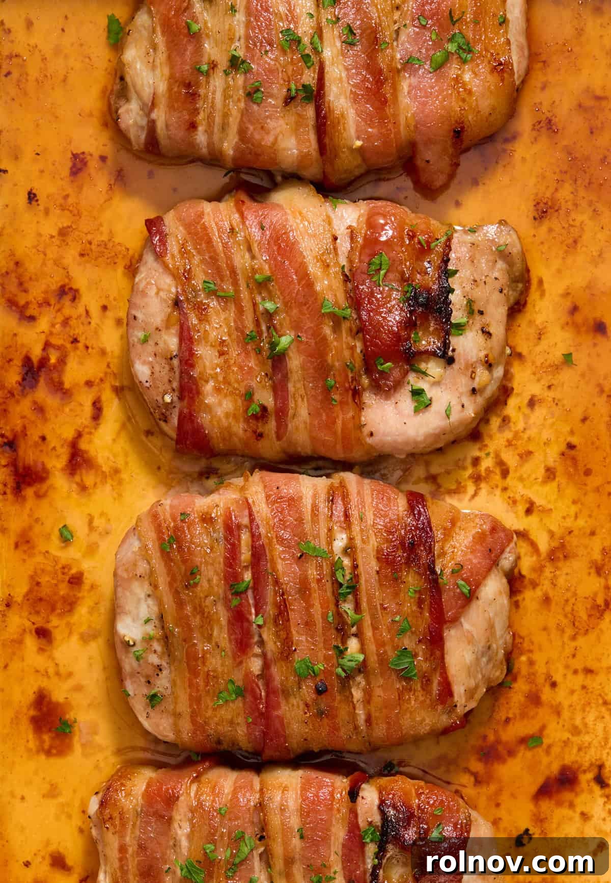Sweet and Savory Maple Bacon Pork Chops 9 Close-up view of perfectly cooked bacon-wrapped pork chops in a pan, garnished with fresh chopped parsley.