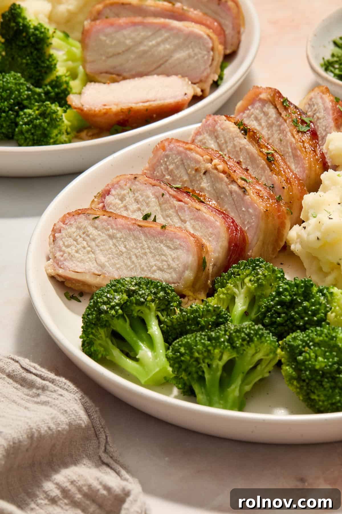 Sweet and Savory Maple Bacon Pork Chops 10 A slice of maple bacon wrapped pork chop on a plate, served with roasted broccoli and mashed potatoes, showcasing the tender interior.