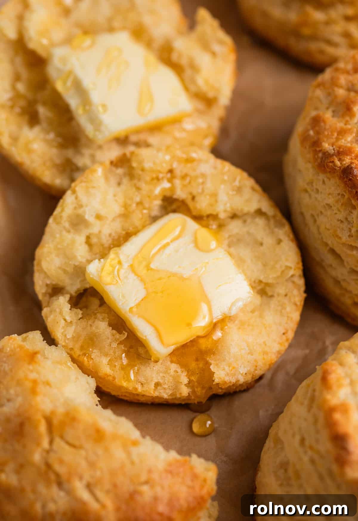 Golden Honey Biscuits 14 A split honey biscuit showcasing its flaky interior, with a pad of butter melting on top and a drizzle of honey.
