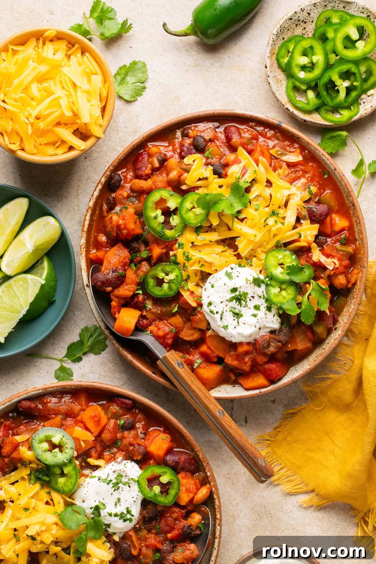 A vibrant bowl of Slow Cooker Sweet Potato Chili, garnished with shredded cheese, a dollop of sour cream, and fresh cilantro, with a spoon ready for a delicious scoop.