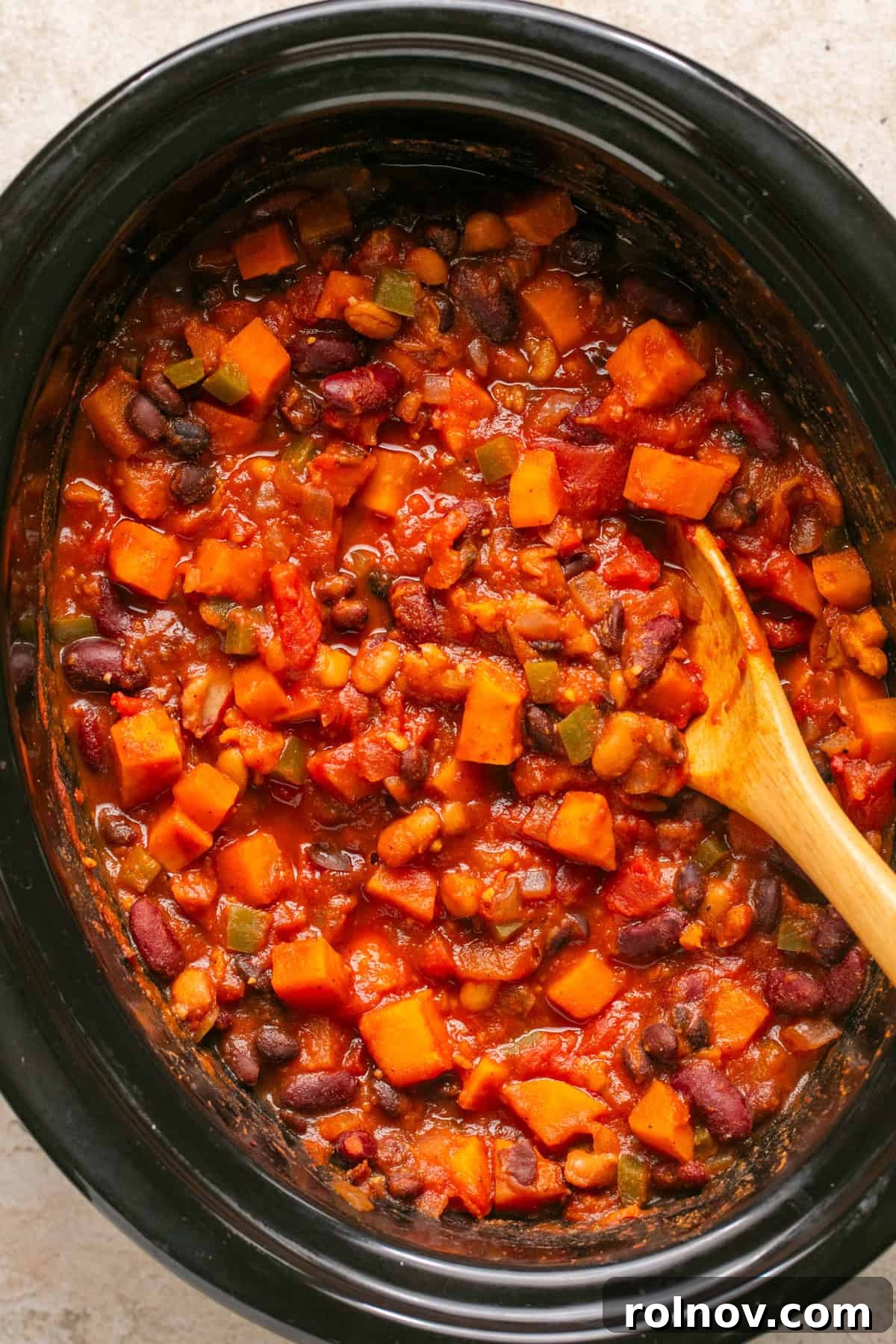 The fully cooked crockpot sweet potato chili, rich and thick, with a wooden spoon resting inside, ready to be served.
