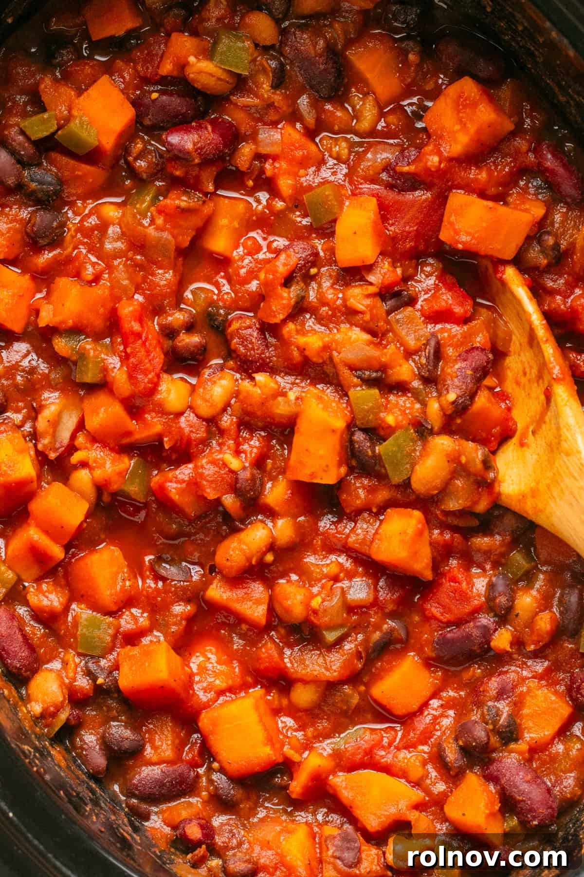 A close-up view of the rich, cooked slow cooker sweet potato chili in the crockpot, with a wooden spoon nestled in the center.
