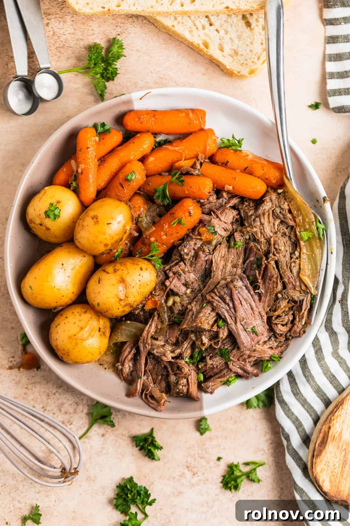 Slow Cooker Beef Pot Roast 10 White plate with chunks or feef, cooked baby carrots, potatoes and onions topped with chopped fresh parsley.