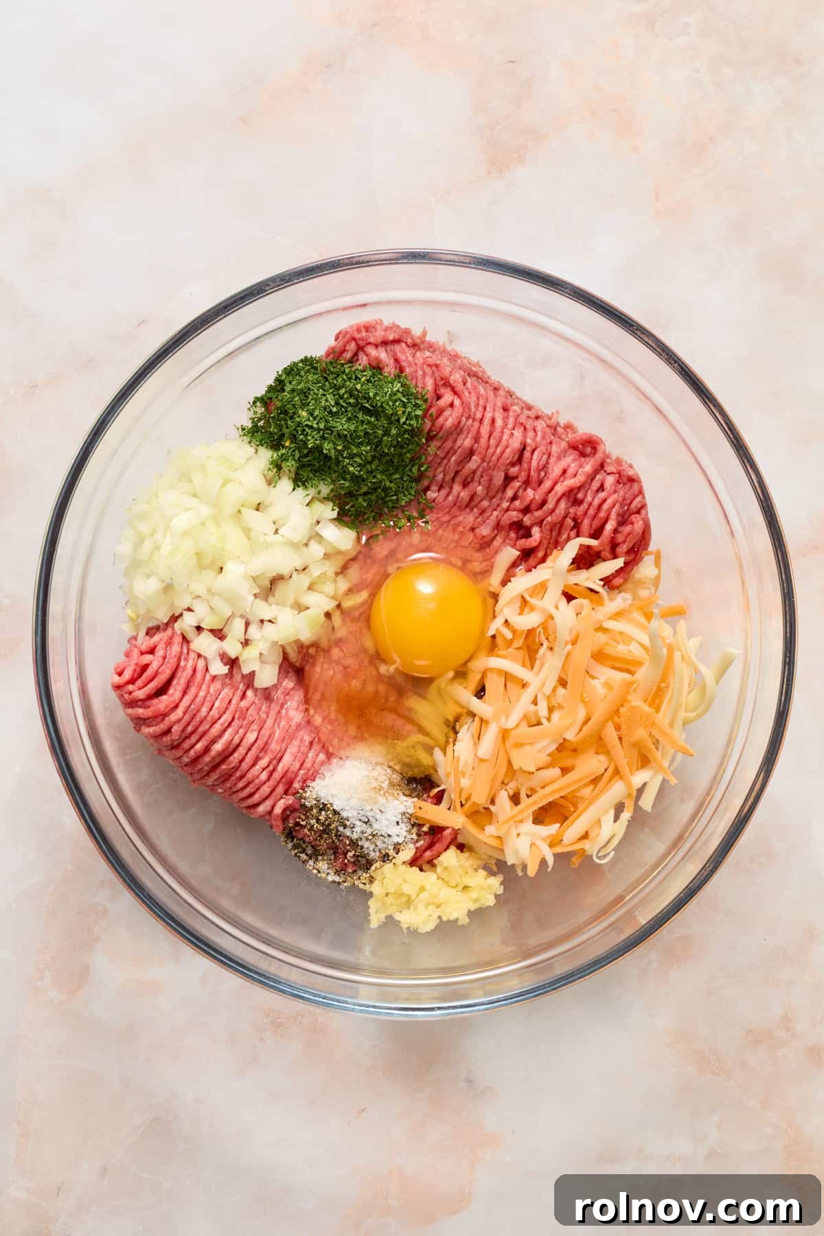 The Ultimate Air Fryer Burger 4 Ground beef, egg, cheese, onion, and various seasonings are placed in a glass mixing bowl, ready to be combined for homemade burger patties.