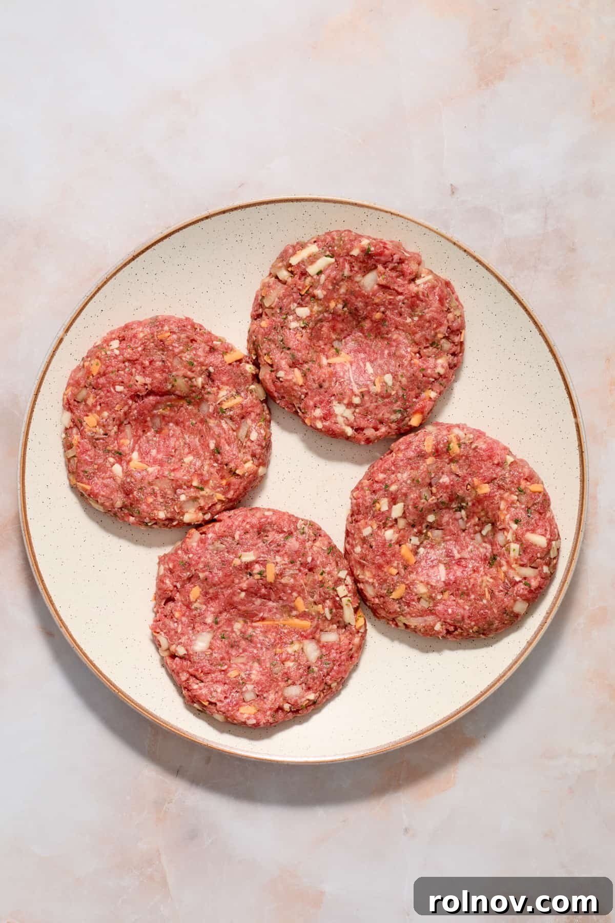 The Ultimate Air Fryer Burger 6 Four perfectly formed hamburger patties with a small indentation in the center, arranged on a plate and ready for chilling before cooking.