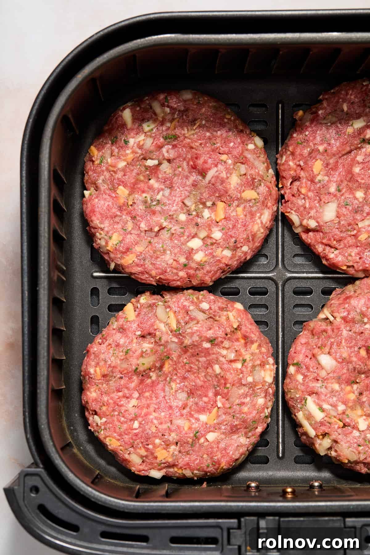 The Ultimate Air Fryer Burger 7 Uncooked hamburger patties neatly arranged in a single layer within the air fryer basket, perfectly spaced for optimal cooking.