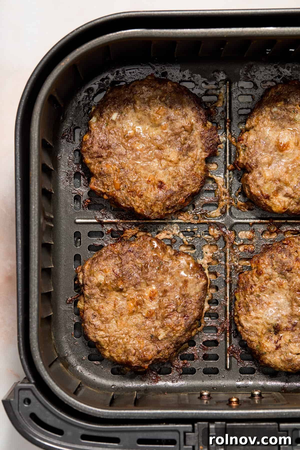 The Ultimate Air Fryer Burger 8 Golden-brown, perfectly air-fried hamburger patties resting in the air fryer basket after cooking, showcasing their juicy texture.