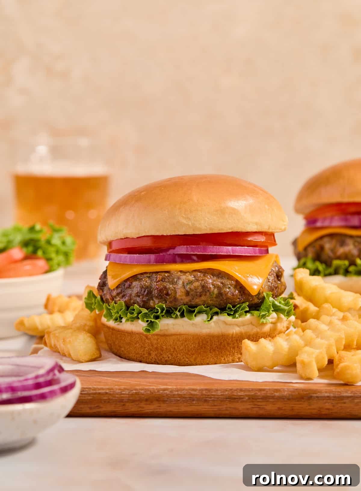 The Ultimate Air Fryer Burger 10 A perfectly cooked air fryer burger, adorned with melted cheese, crisp lettuce, red onion, and fresh tomato, served on a toasted bun with a side of golden fries and a refreshing beverage in the background.