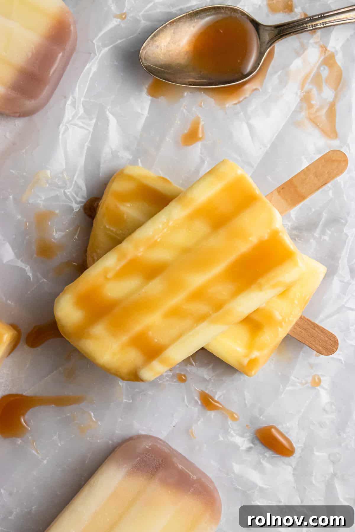 DIY Jello Pudding Pops 5 Overhead view of several homemade Jello Pudding Pops, some with a caramel drizzle, on a white surface.