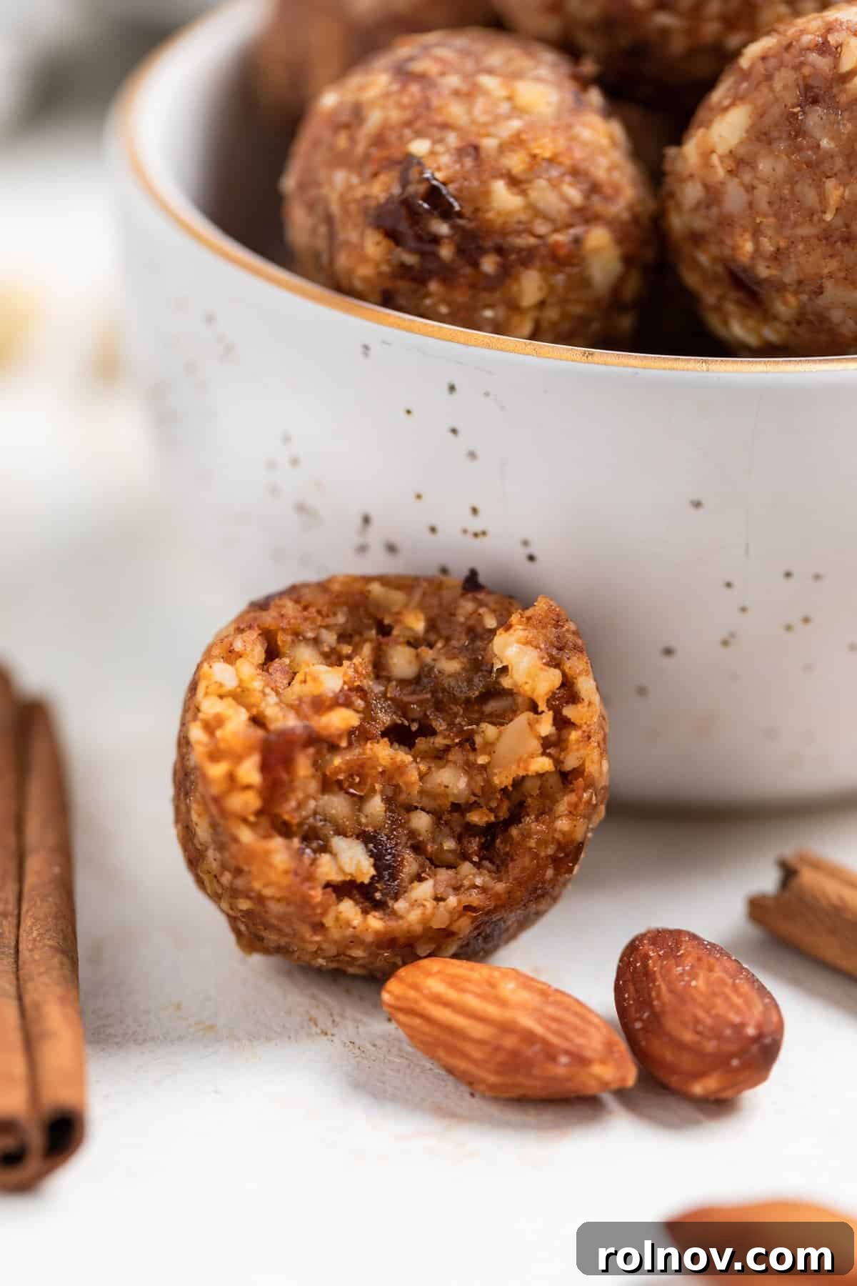 Pumpkin Spice Power Bites 3 A perfectly formed pumpkin pie energy bite with a small segment missing, indicating its delicious texture. It rests invitingly next to a bowl brimming with more of these healthy, no-bake treats.