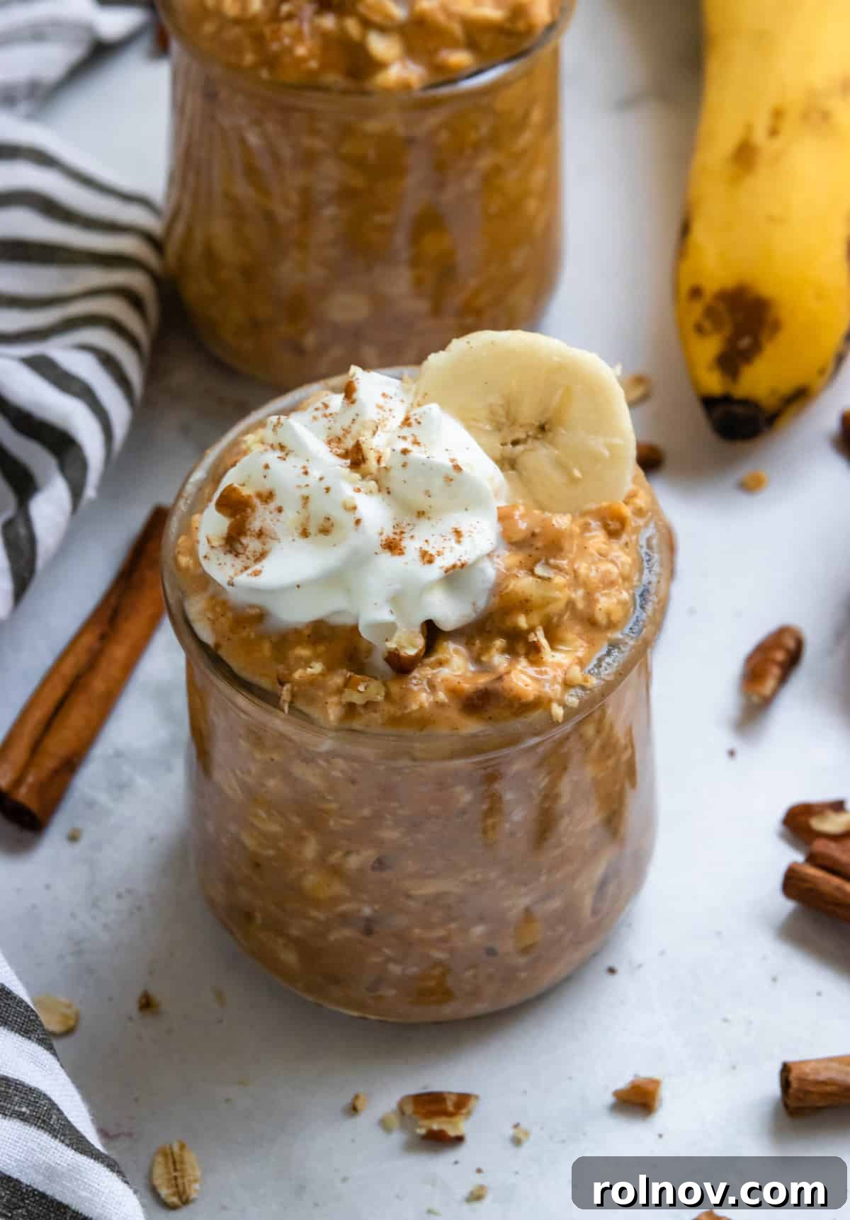 Golden Pumpkin Banana Overnight Oats 2 Pumpkin banana overnight oats in jars with banana slices and whipped cream.