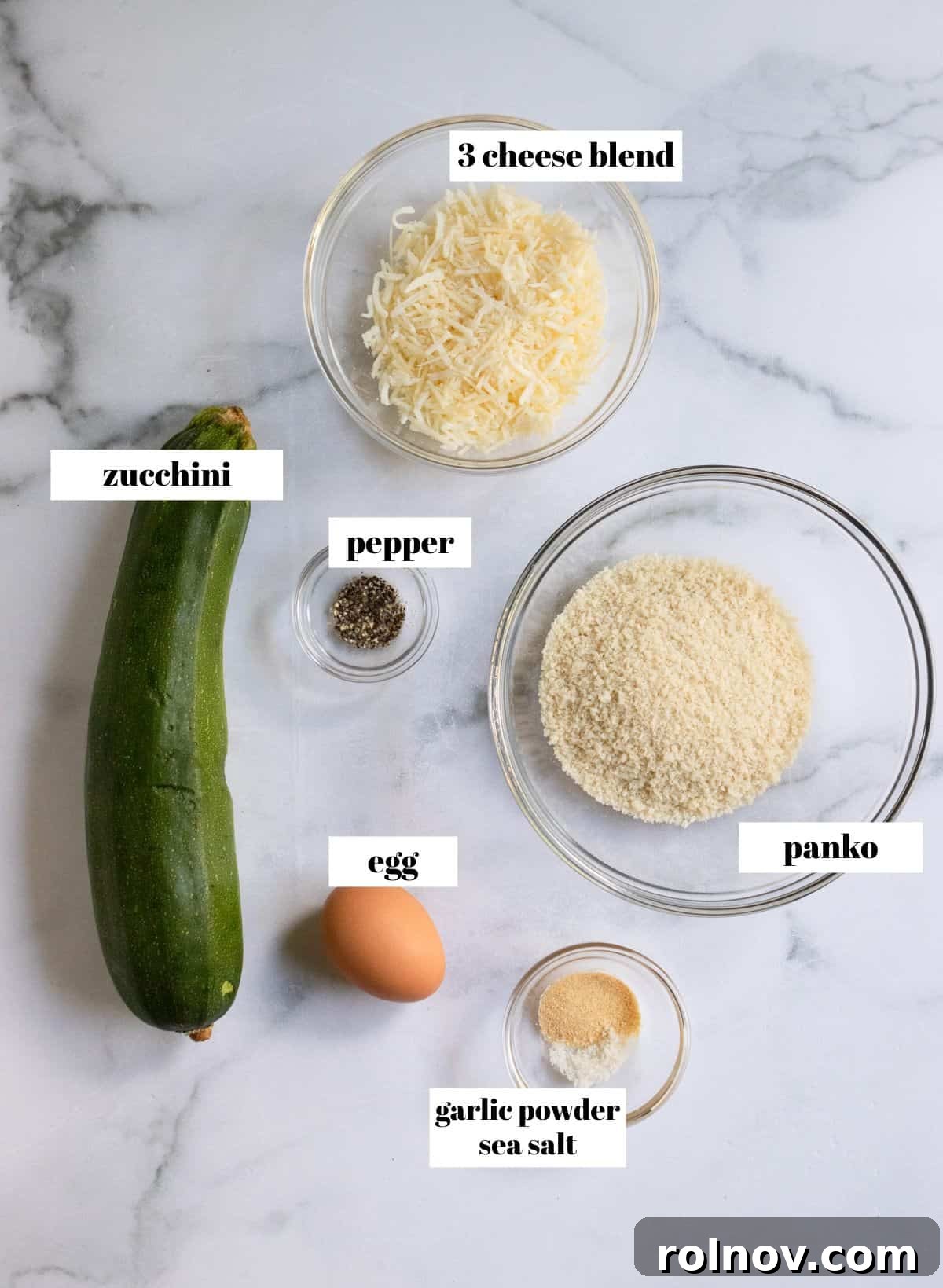 Crispy Three Cheese Air Fryer Zucchini 3 Individual ingredients like zucchini, panko, cheese blend, and seasonings laid out on a white surface, ready for the recipe.