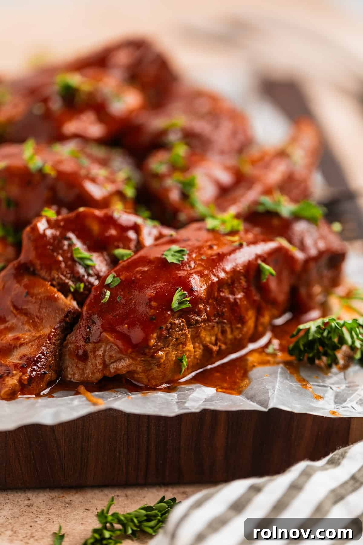 Slow Cooker BBQ Country Style Ribs 2 Country style BBQ ribs served on a wooden board lined with wax paper and garnished with fresh parsley.