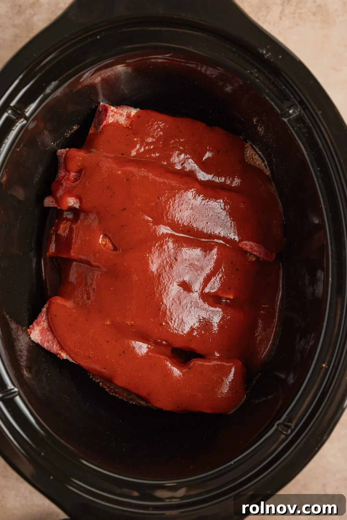 Slow Cooker BBQ Country Style Ribs 6 BBQ sauce being generously poured over boneless pork ribs in a slow cooker.