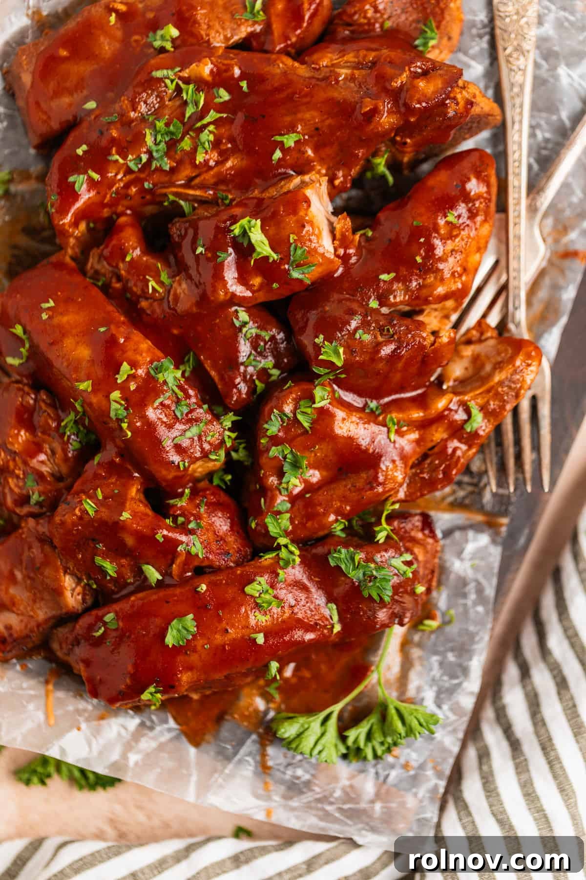 Slow Cooker BBQ Country Style Ribs 8 Slow cooker country ribs topped with a rich layer of BBQ sauce and fresh chopped parsley, displayed on a wooden cutting board lined with wax paper.