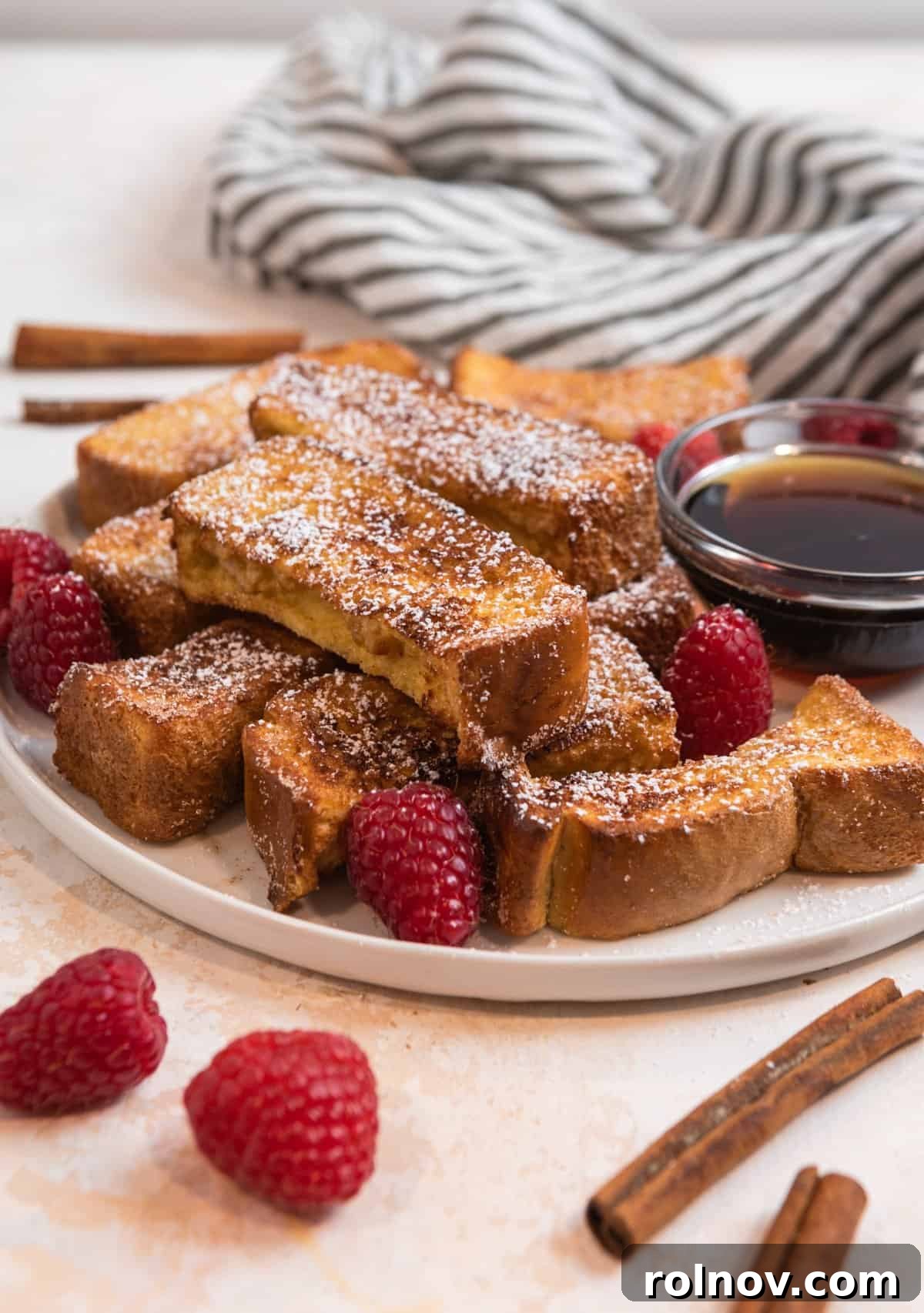Crispy Air Fryer French Toast Sticks 2 Crispy Air Fryer French Toast sticks dusted with powdered sugar and garnished with fresh raspberries on a white dish, ready for a delightful breakfast.
