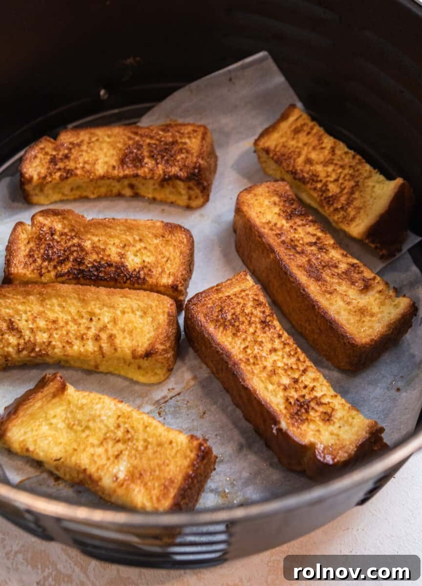 Crispy Air Fryer French Toast Sticks 7 Cooked French toast sticks, golden and crispy, perfectly arranged in an air fryer basket after being air-fried, showcasing their delicious texture.