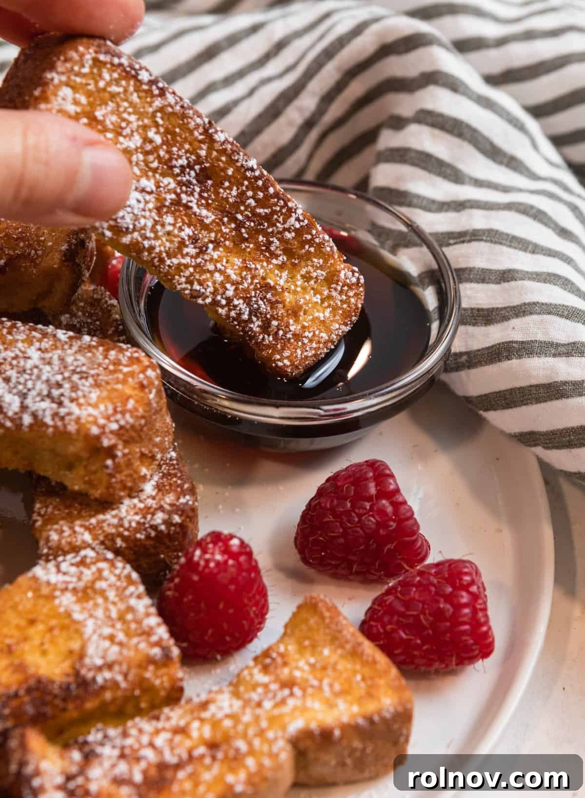Crispy Air Fryer French Toast Sticks 9 A delicious Air Fryer French toast stick being gently dunked into a small glass dish filled with golden maple syrup, highlighting its perfect coating and readiness to be enjoyed.