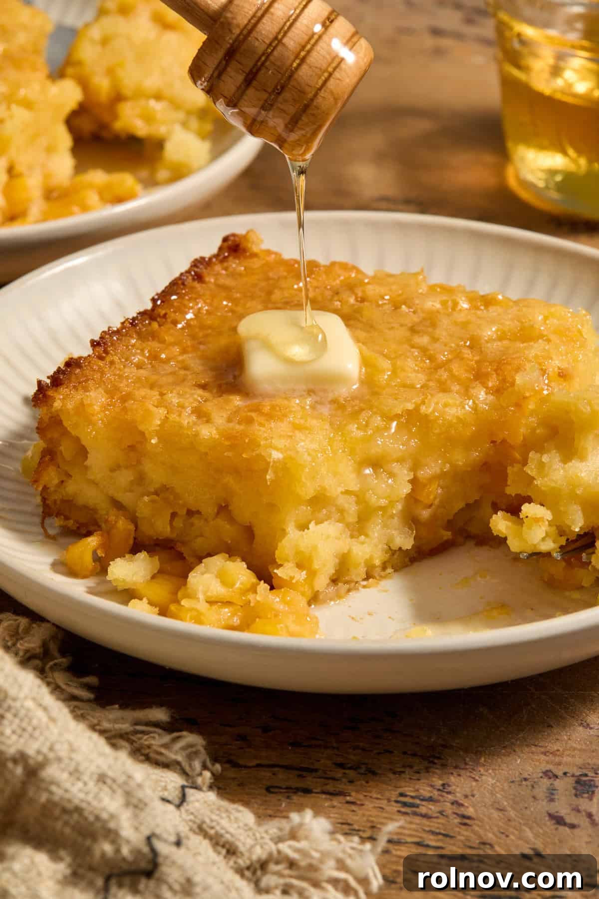 Golden Honey Cornbread Bake 2 Honey cornbread casserole served on plate with honey drizzling over butter on top.
