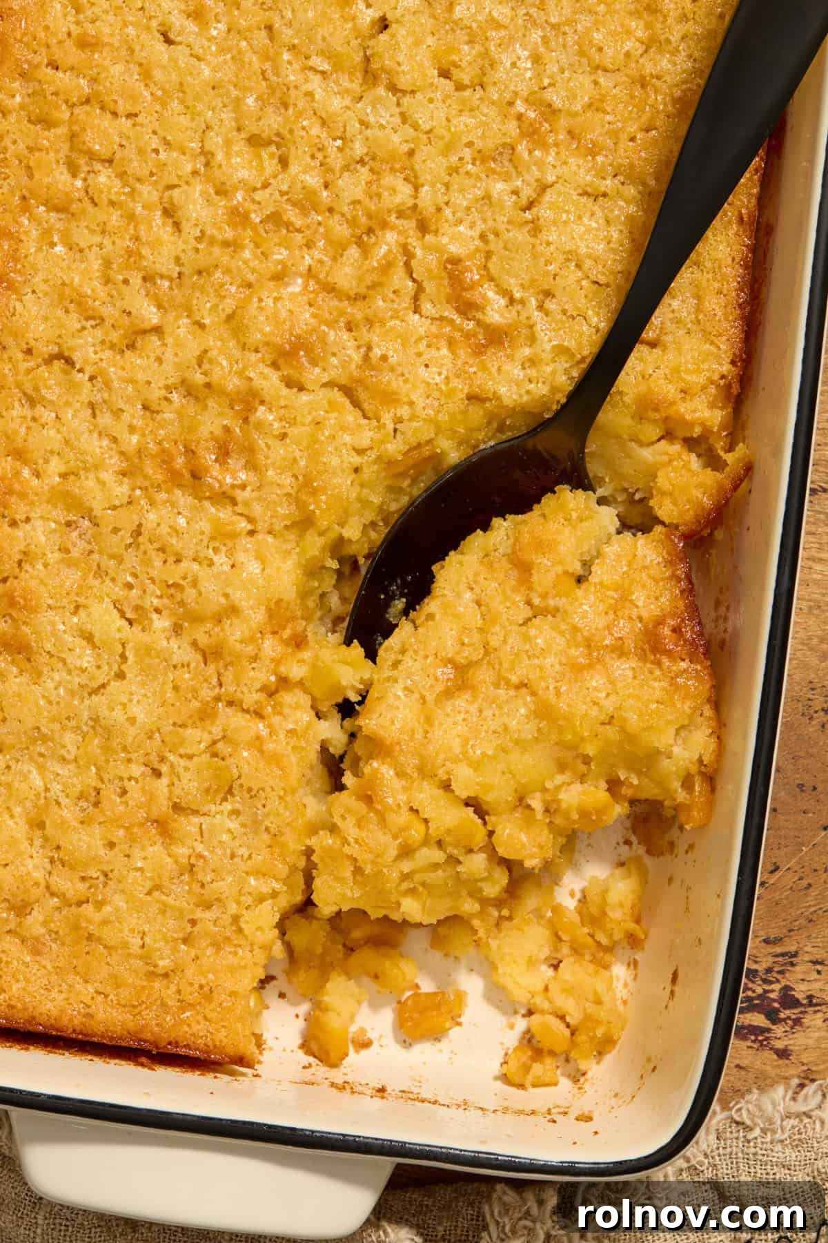 Golden Honey Cornbread Bake 11 Cornbread casserole in dish with serving spoon scooping in.