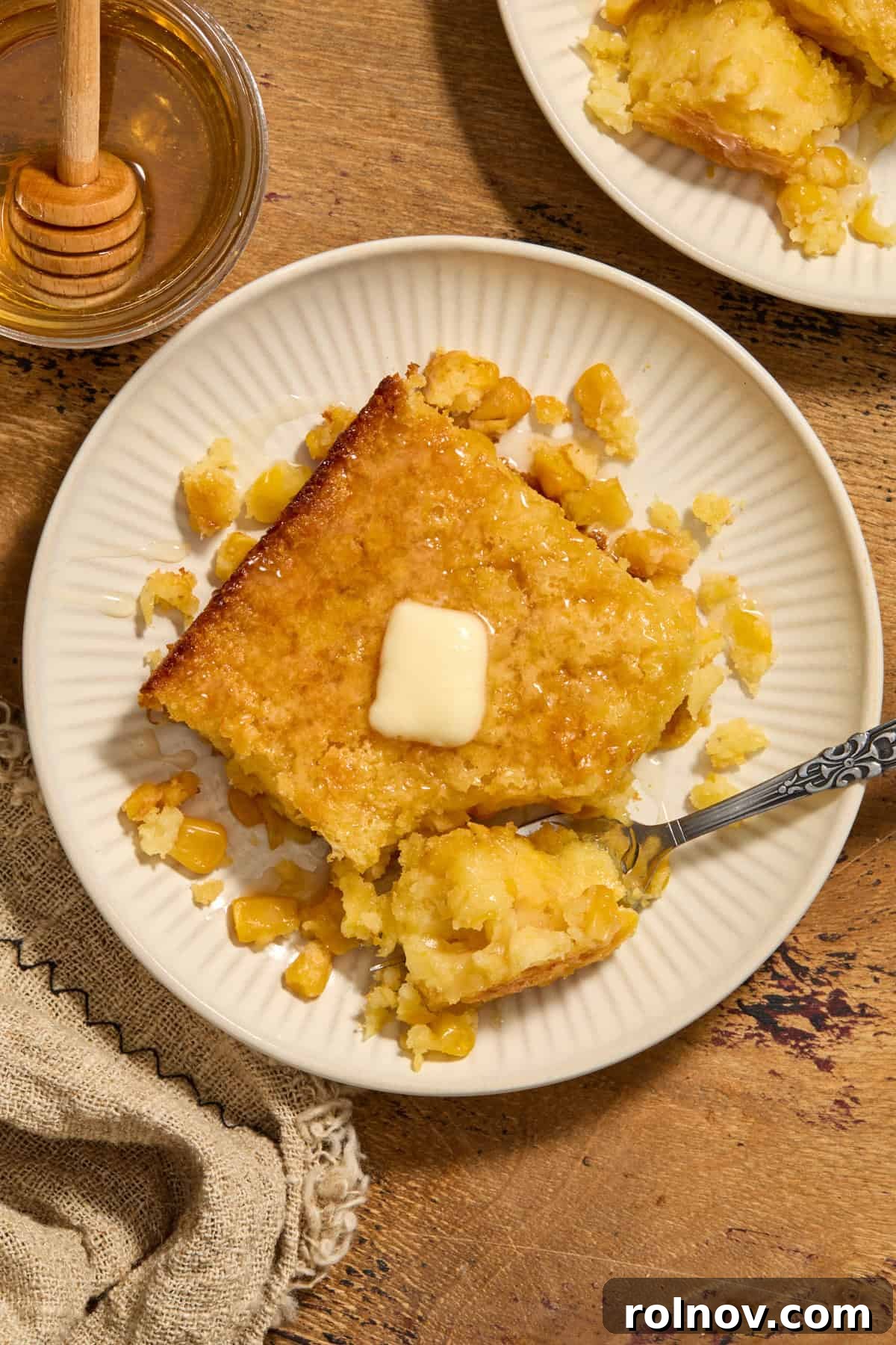 Golden Honey Cornbread Bake 12 Serving of cornbread casserole on plate with butter and honey on top.