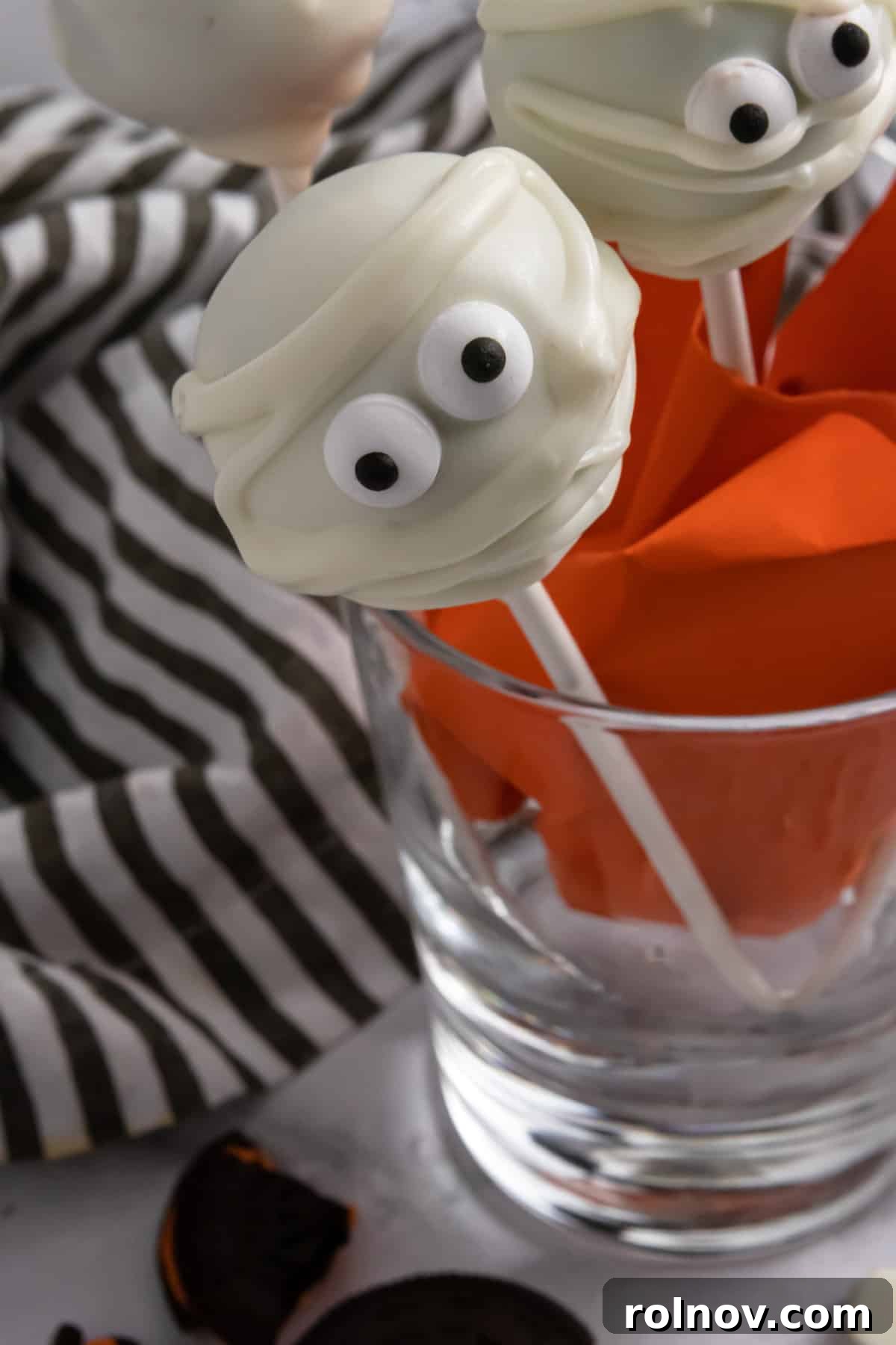 Vibrant Halloween cake pops arranged artistically in a glass cup, ready for a spooky celebration.