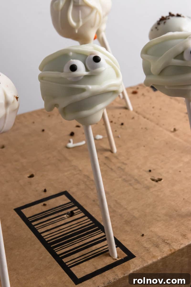 A selection of decorated Halloween cake pops, including spooky monster eyes and mummy designs, displayed upright.