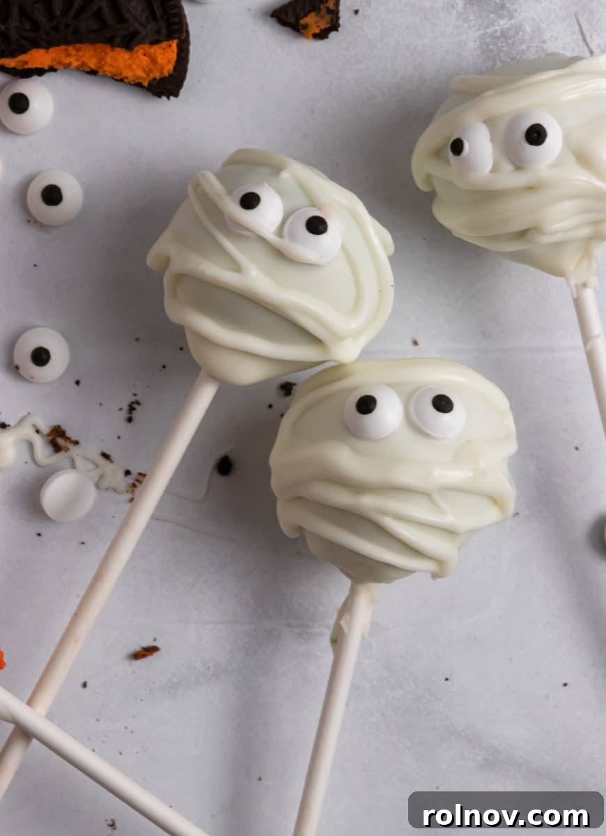 A festive assortment of Halloween cake pops, adorned with various spooky decorations, displayed on a kitchen counter, ready for a party.