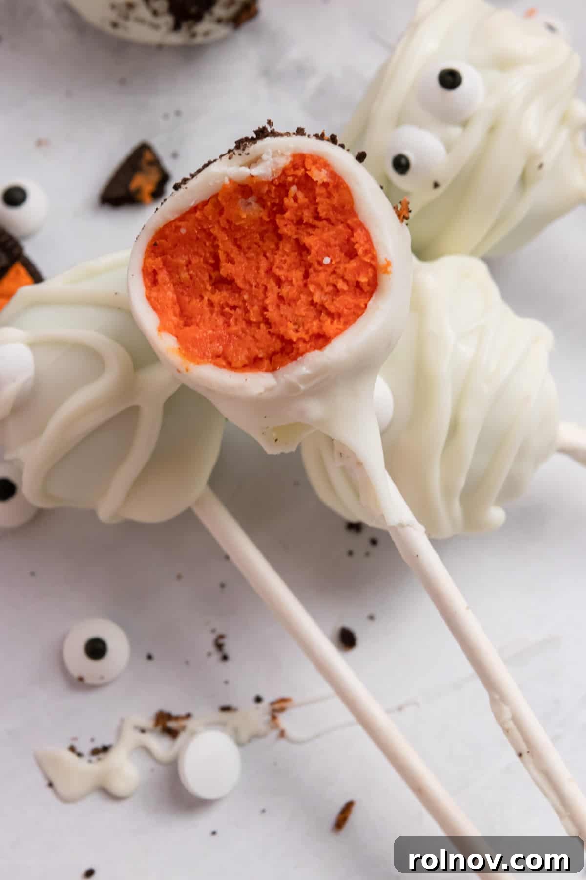 A Halloween cake pop with a bite taken out, revealing a vibrant orange interior, showcasing the delightful texture and color within.