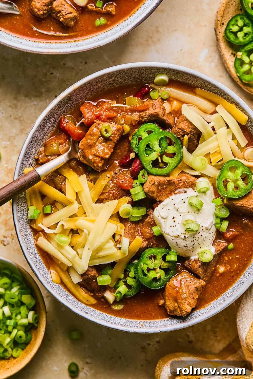 A hearty bowl of slow cooker beef brisket chili, generously topped with shredded cheese, a dollop of sour cream, and fresh green onions, ready to be enjoyed.