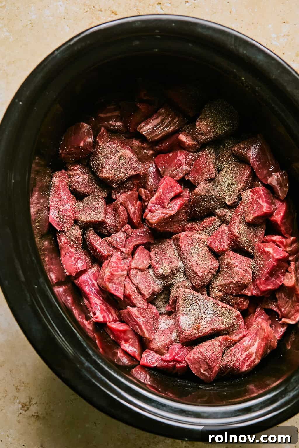 Cubed beef brisket seasoned and ready in the slow cooker pot.