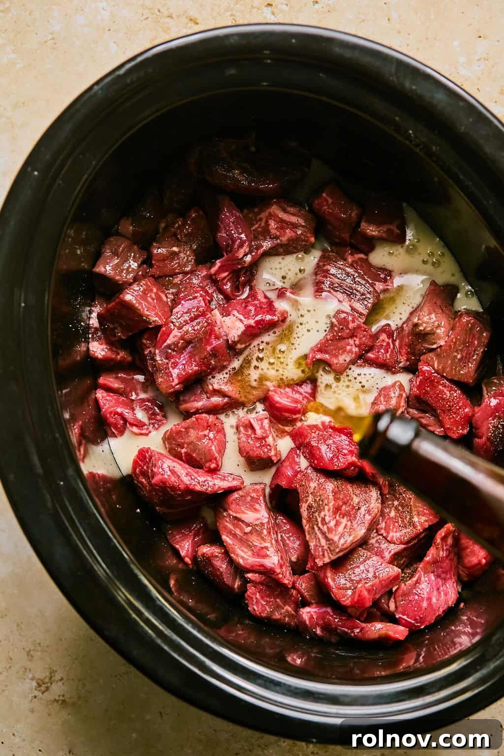 A can of IPA beer being poured over the seasoned beef brisket in the slow cooker.