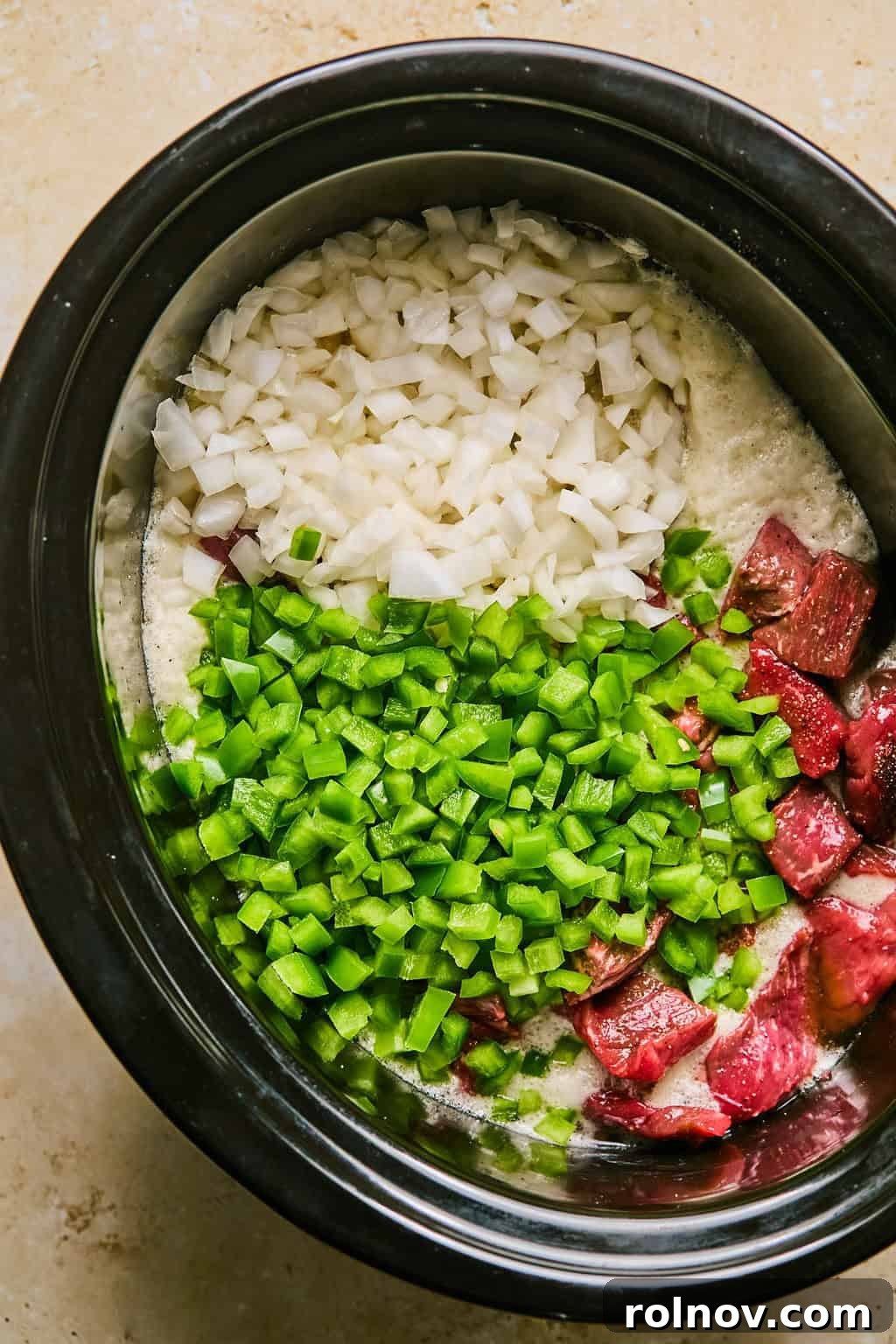 Chopped green bell peppers and onions layered over the brisket in the slow cooker.