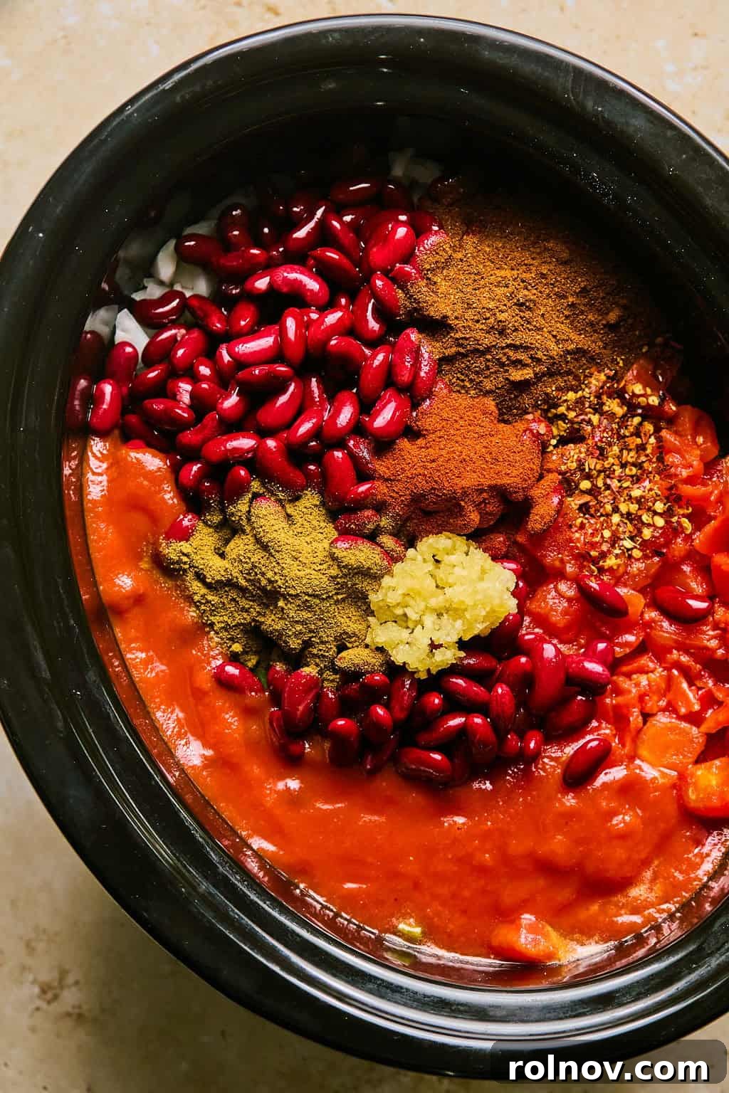 Kidney beans, diced tomatoes, garlic, and spices added on top of the vegetables in the slow cooker.