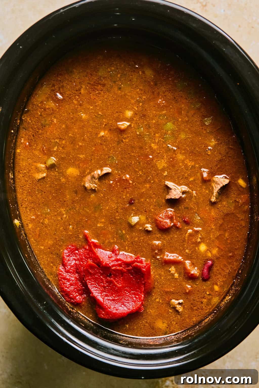 Cooked beef brisket chili in the slow cooker with tomato paste being stirred in for thickening.