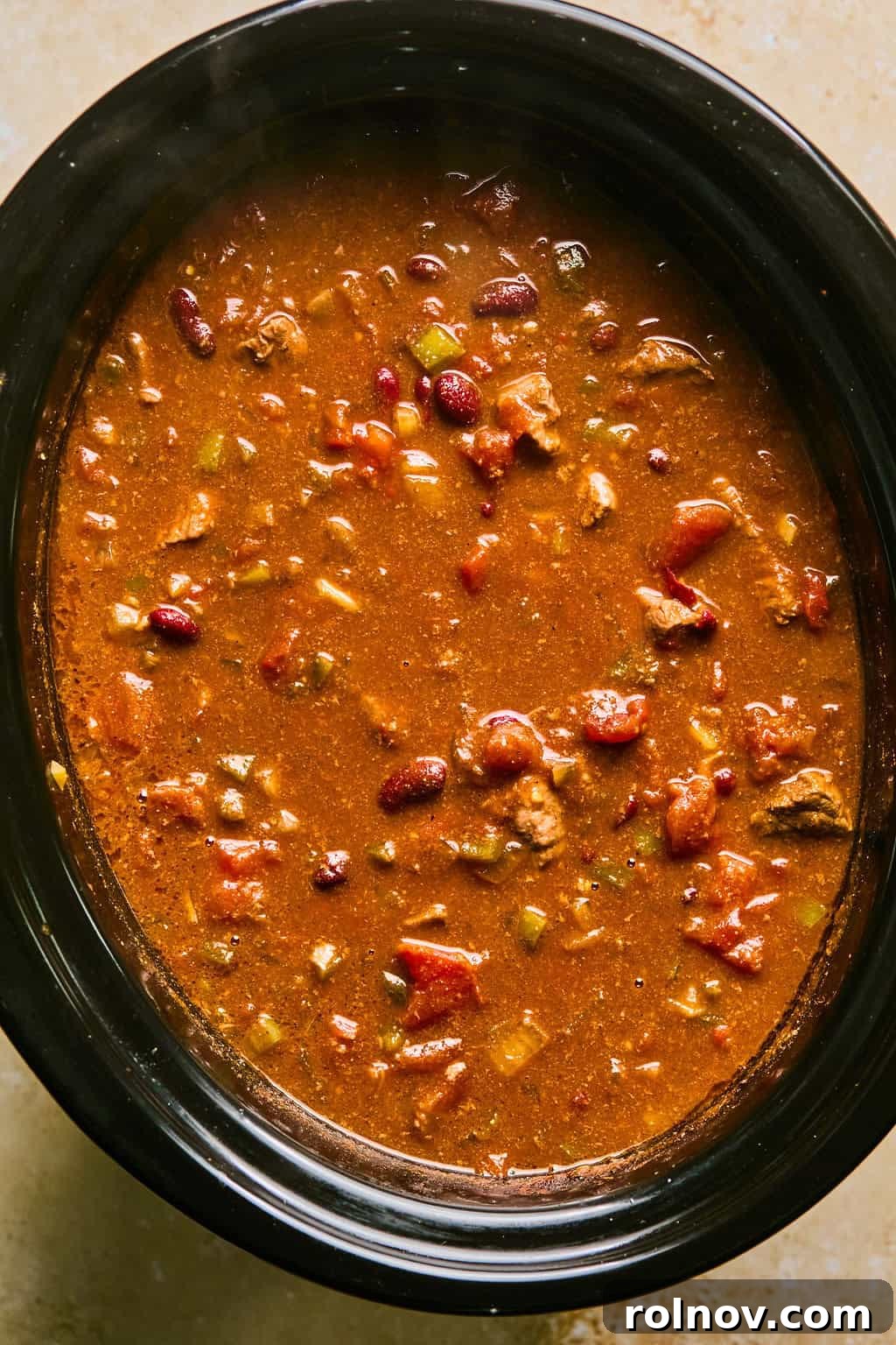 A full crockpot of finished, richly colored beef brisket chili, ready to be served.