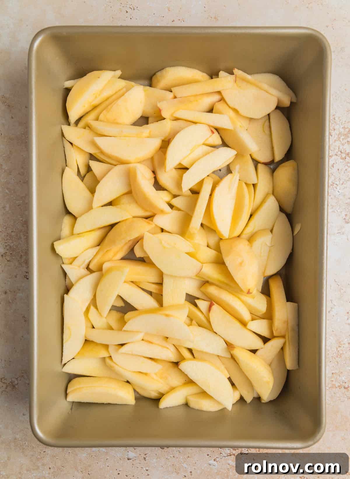 Effortless Golden Apple Bake 4 Peeled, uniformly sliced apples arranged in a single layer within a baking pan, ready for seasoning.