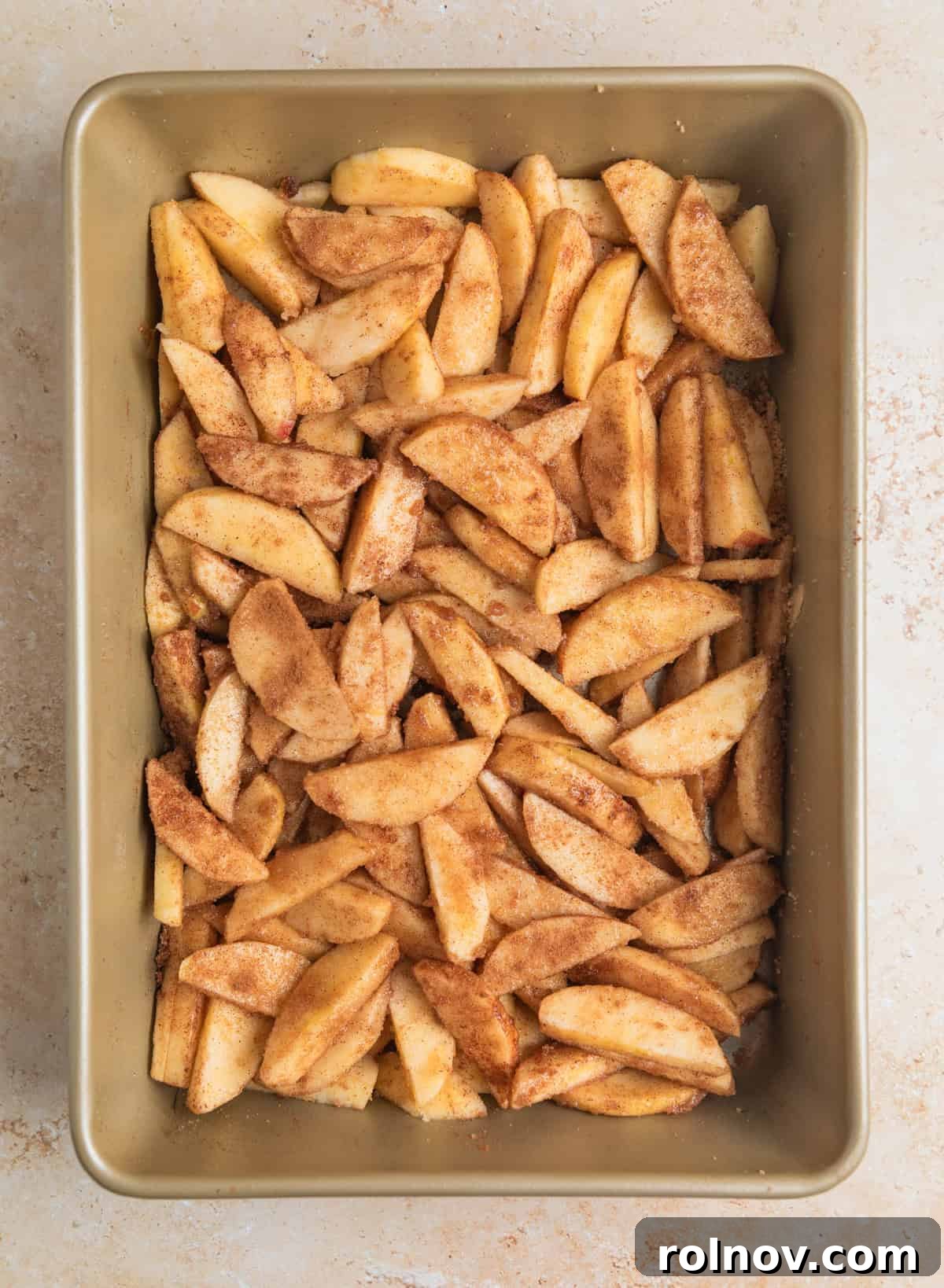 Effortless Golden Apple Bake 6 Apples thoroughly coated with cinnamon and sugar mixture, glistening in the baking pan, preparing for the next layer.