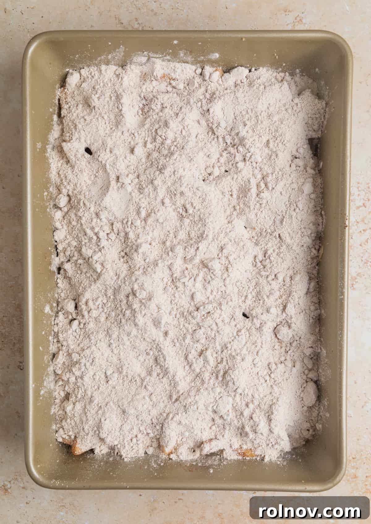 Effortless Golden Apple Bake 7 Dry spice cake mix evenly sprinkled over the cinnamon-sugar coated apples in the baking pan, forming the next layer.