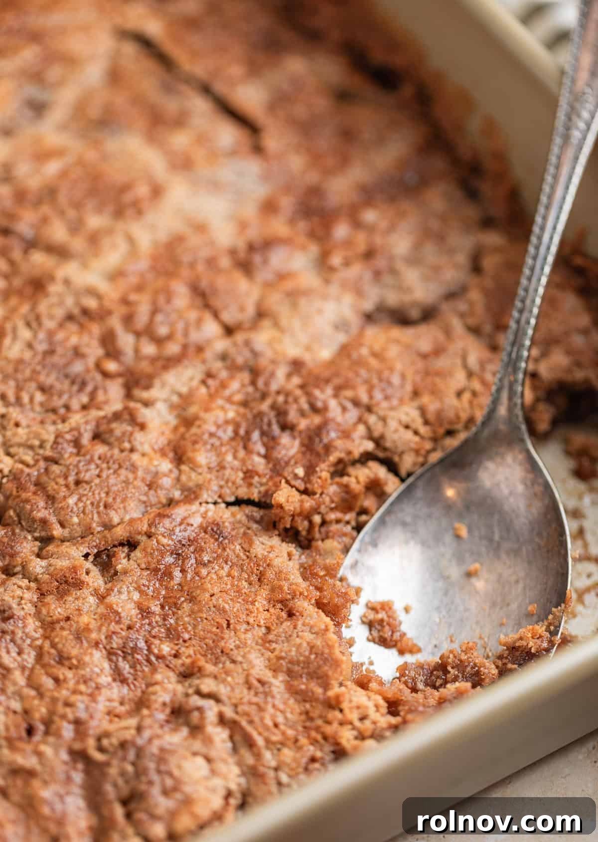 Effortless Golden Apple Bake 10 Serving spoon scooping into a pan of freshly baked apple dump cake, highlighting its warm, gooey texture and inviting aroma.