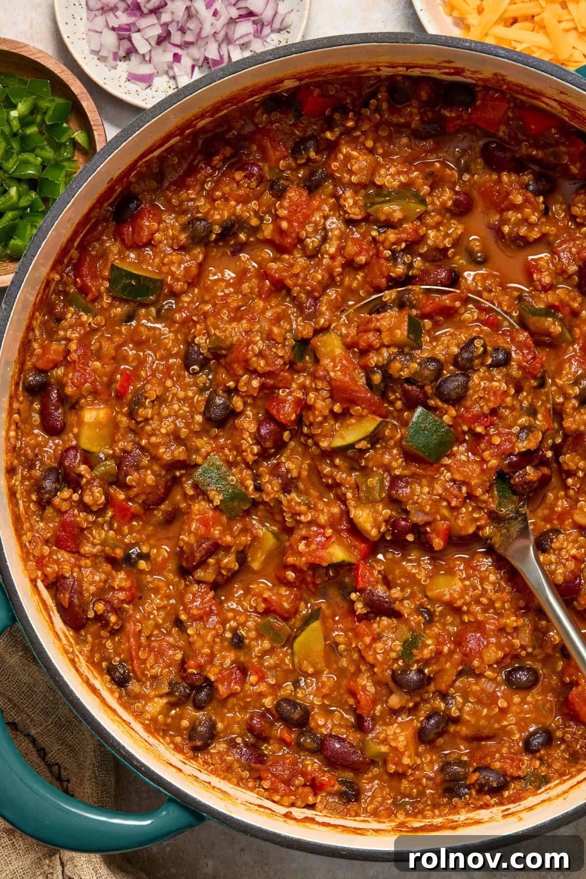 A rustic pot filled with vibrant pumpkin quinoa chili, ready to be served, with a ladle resting inside.