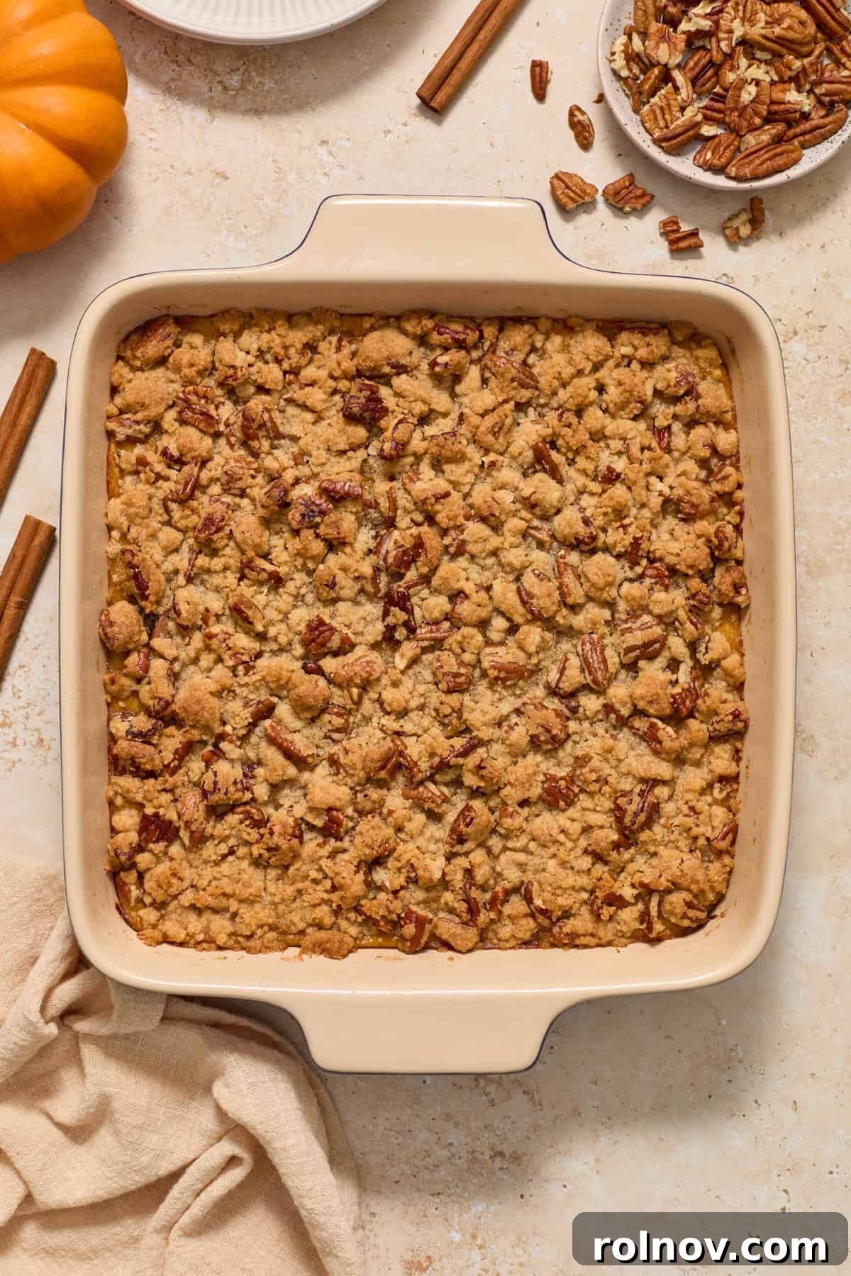 A beautifully baked crumble-topped butternut squash casserole, garnished with cinnamon sticks and autumn leaves, evoking cozy fall vibes.
