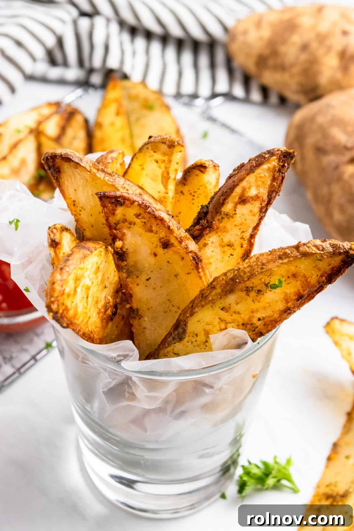 Crispy air fried potato wedges served upright in a glass, ready to be dipped in ketchup.