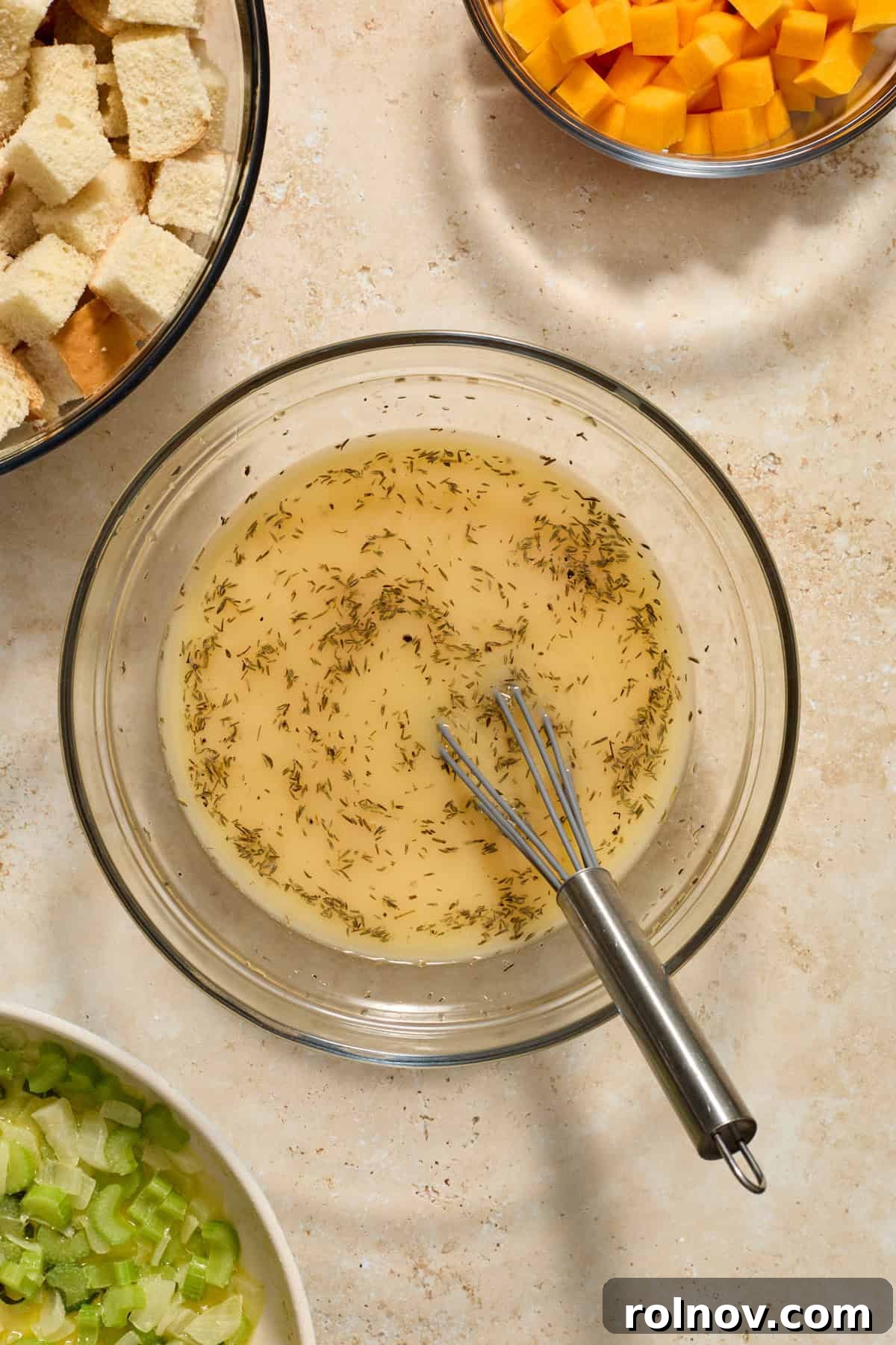 A glass mixing bowl with whisked chicken broth, eggs, and herbs, ready to be combined with other ingredients.