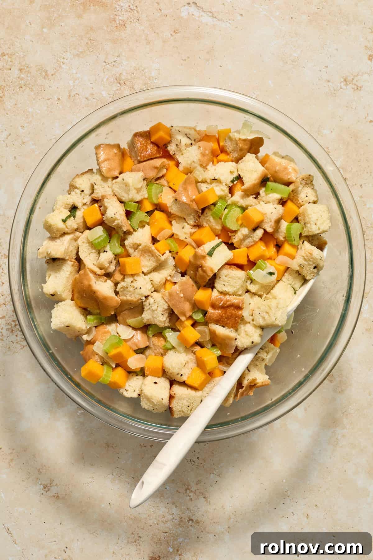 Prepared stuffing mixture in a large glass bowl before being transferred to a baking pan, showing all ingredients combined.