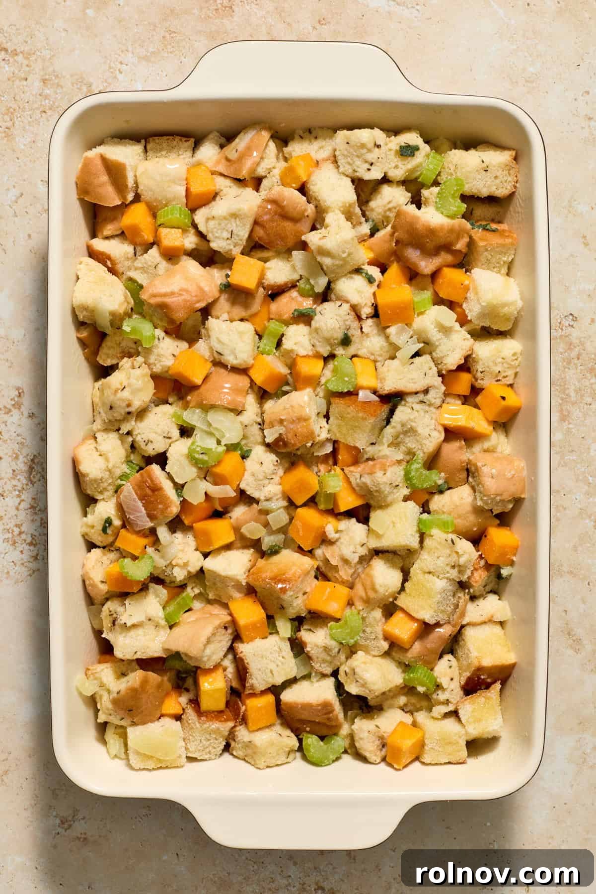 A baking pan filled with uncooked stuffing ingredients, with melted butter drizzled generously over the top, ready for the oven.