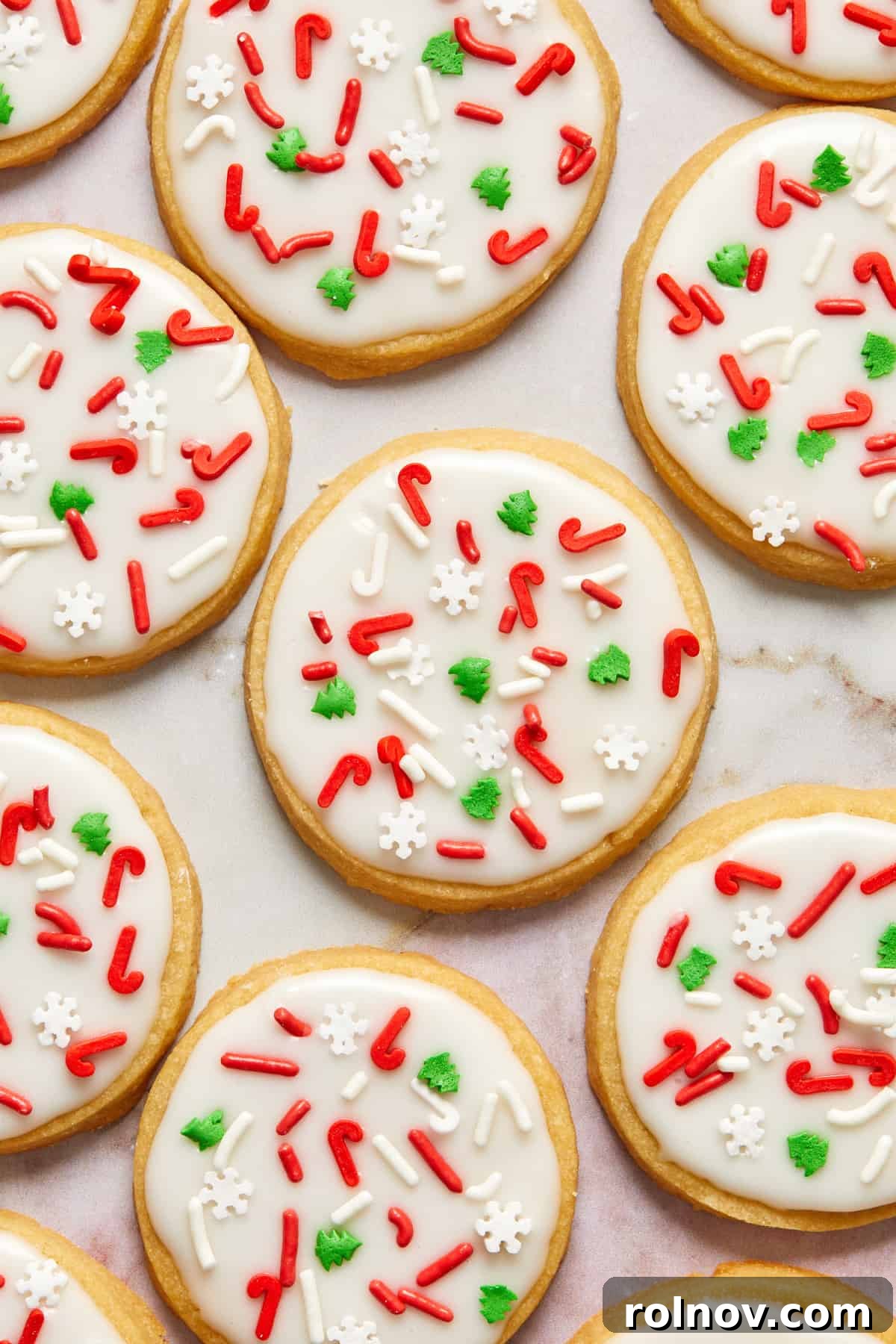 Buttery Holiday Shortbread Delights 2 Christmas shortbread cookies with white icing and red and green holiday sprinkles arranged on counter.