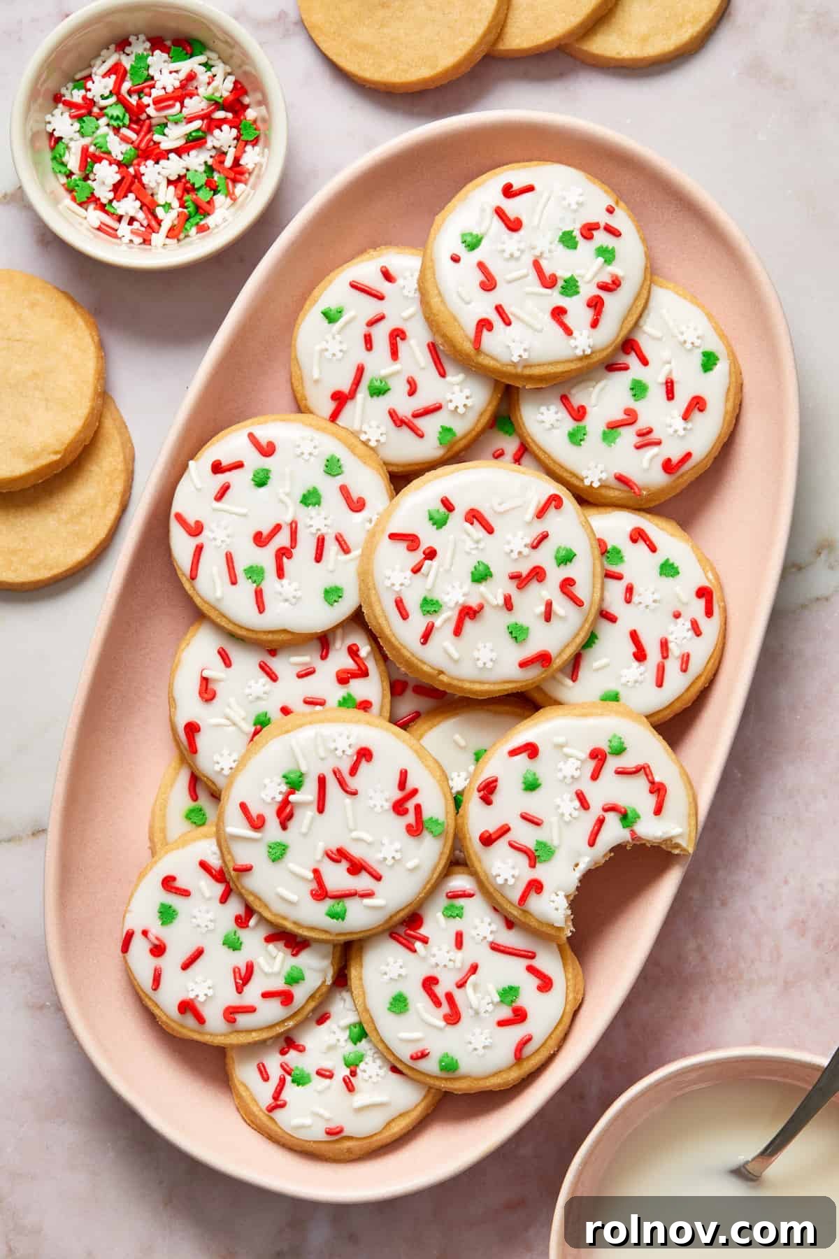 Buttery Holiday Shortbread Delights 12 Pink dish filled with iced shortbread cookies with red and green sprinkles.