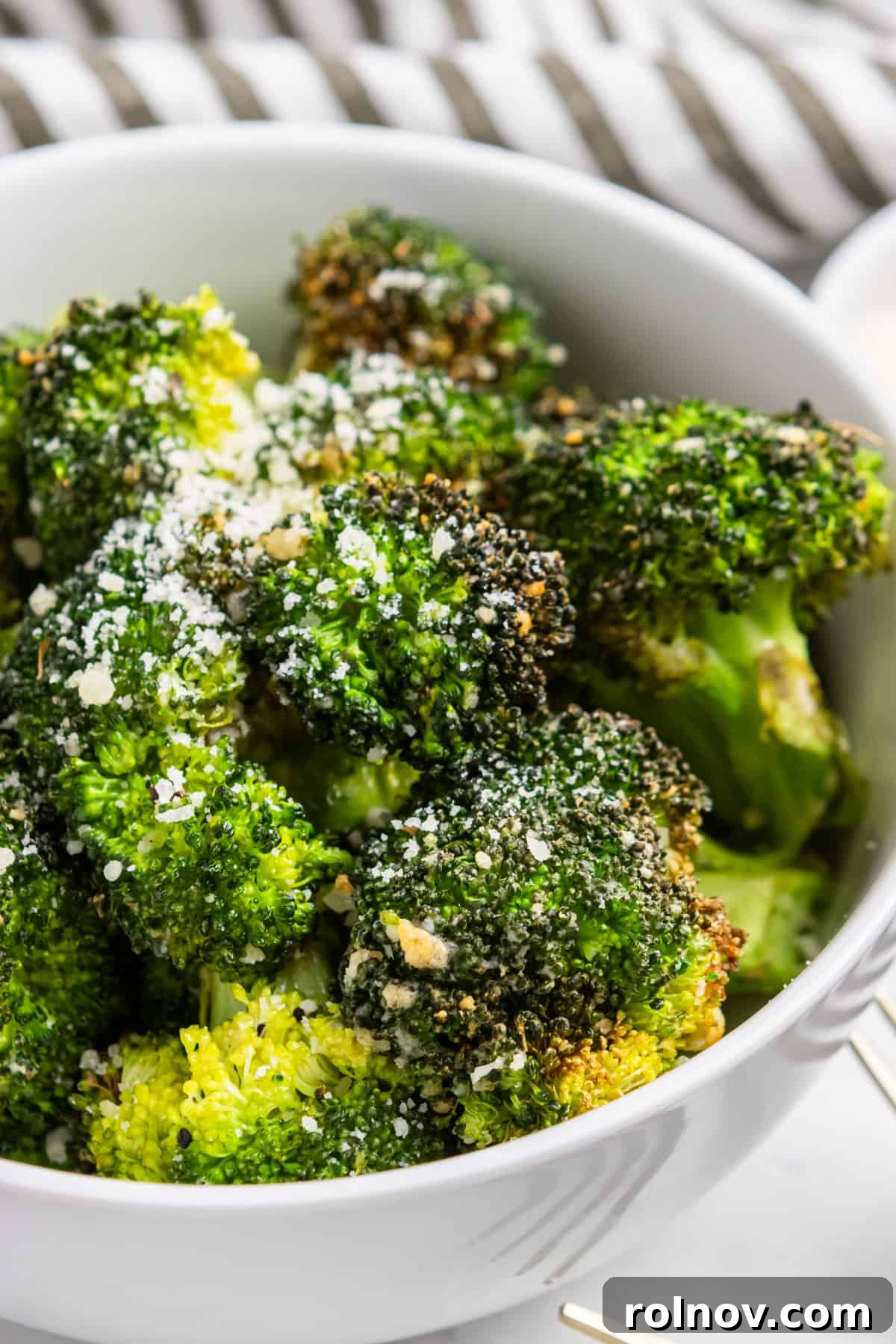 Easy Crispy Air Fryer Broccoli 2 A bowl of freshly air-fried broccoli florets generously topped with grated Parmesan cheese, ready to be served.